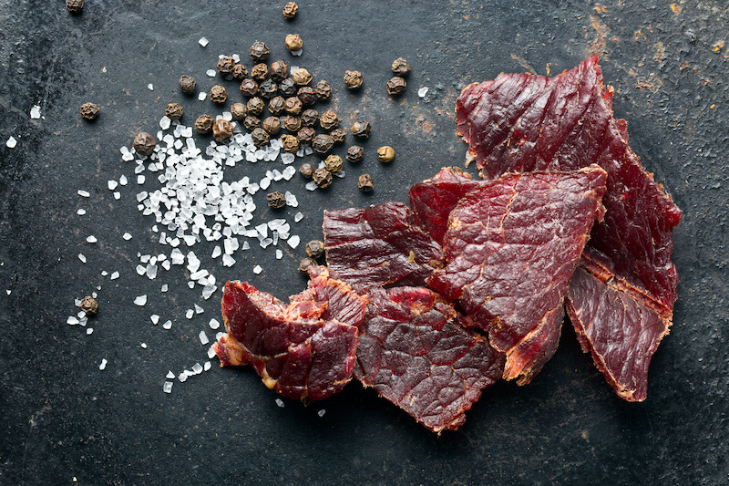 beef jerky and spices on a marble cutting board showing how cured meat can be tender from meat massaging technology