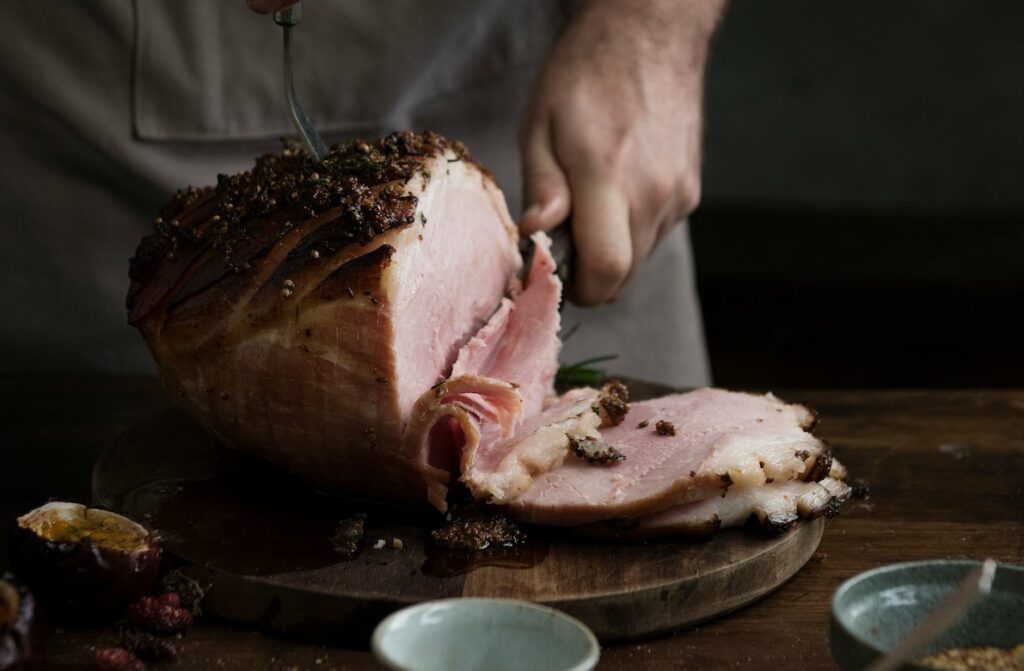 Delicious-looking cooked ham being sliced on a wood board with bowls of condiments around showing a product made using Massaging and Tumbling Equipment